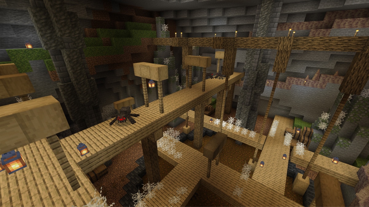 木の足場とレールが組まれた地下の廃坑を、ランタンが照らしているMinecraftの場面